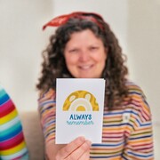 Lady in a stripy top holding out a colourful motivational card with a rainbow