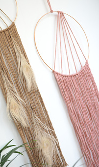 two macrame wall hangings in pink and beige with peacock feathers
