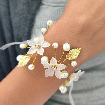 This is a beautiful and intricate wedding corsage. The corsage features delicate white flowers adorned with golden leaves and pearls, all connected by slender g