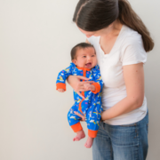 Image of a mum cuddling a baby. The baby is wearing a colourful Ducky Zebra zip-up romper