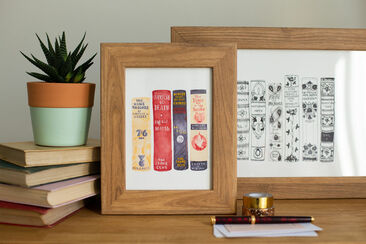 Two book spine artworks, in oak frames, displayed next to a stack of books.