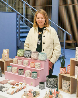 Image of Kelly, the owner and maker behind Slow Make Studio. Kelly is standing behind her market stall, which features colourful plant pots, soap dishes etc.