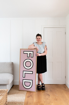 A white female is standing by a large sign, which says FOLD.