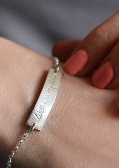 Close up of a silver bracelet with a curved bar which has handwriting engraved on it. The writing reads 'with all my love'.