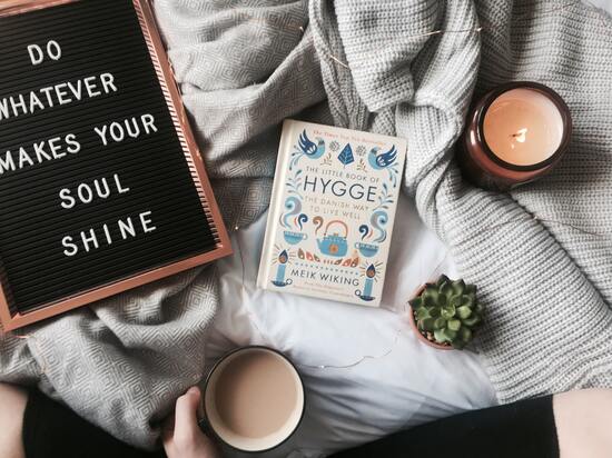 Hygge book on a blanket with a candle, a succulent plant and a cup of tea. There is a board with the quote do whatever makes your soul shine.