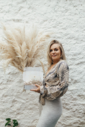 Pampas grass being held with Naked Palm Jewellery's packaging. Hands include gold rings. Full portrait image of founder Toriee. Neutral aesthetic.
