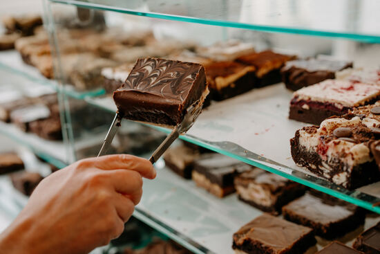 a hand holding tongs and a millionaires brown in front of a counter full of brownies