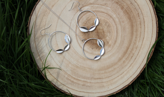 Sterling silver hoop drop earrings with leaves and matching pendant on chain on a wooden slice in the green grass