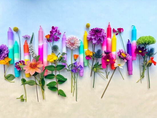 a selection of different coloured dip dyed candles on a blue and beige background in amongst flowers