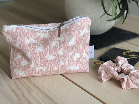 Pink floral beauty pouch sitting on table next to matching scrunchie.