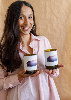 Image of Magali Bellego the maker behind Wax / Wine. She is holding to wine bottle candles and she is wearing a long pink shirt