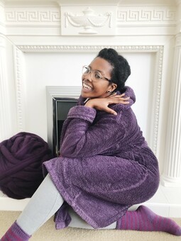 Nadine sitting on the fireplace in her dressing gown with a big ball of wool