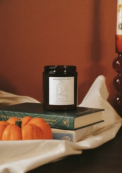 an amber candle called 'moonrise' sits on some books with a pumpkin next to it