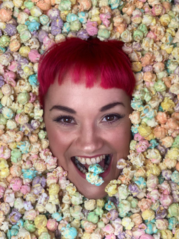A Ladies head with red hair and buried in Rainbow popcorn