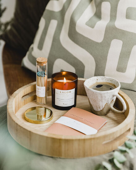 candle burning on a round wooden tray beside a mug of coffee and a jar of matches