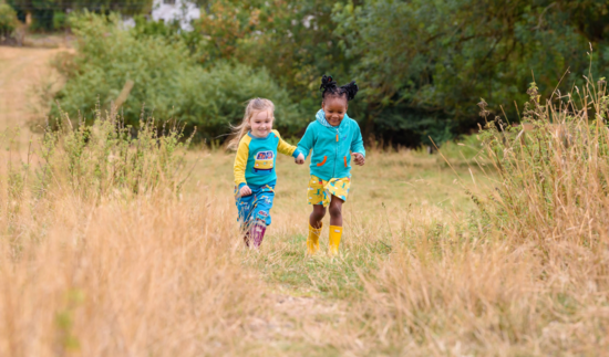 Image of two girls confidently holding hands running through the grass. They're both wearing bright, colourful Ducky Zebra clothes