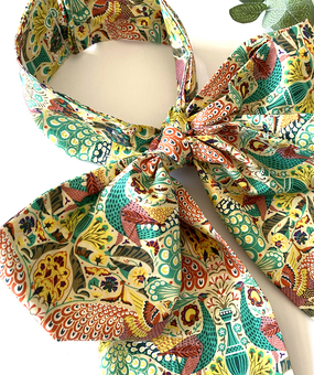 A close up of a detachable pussy bow in a colourful peacock print fabric