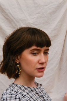 Girl with brunette bob in gingham dress wearing ‘noir earrings’ which look like gold seaweed