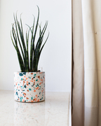 Handmade small plant pot featuring blue and pink terrazzo chips sitting on a window sill with a small plant inside.