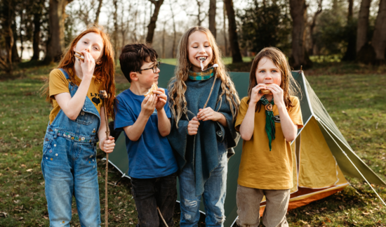 Four children eating marshmallows in front of tent