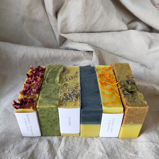 Six bars of colourful soap sit next to each other on a linen fabric background.