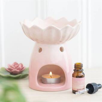 Pink water lily-shaped ceramic oil burner and wax warmer with a lit tealight candle inside, accompanied by a bottle of essential oil and dropper,