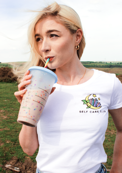 a blonde girl sipping a drink from starbucks wearing a white tshirt with an embroidered image on the left breast. the image is of a moon, leaves and crystals