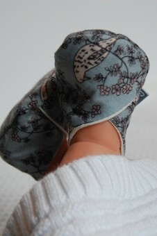 baby feet wearing a pair of slippers in blue-grey recycled fabric with a bird and flower print