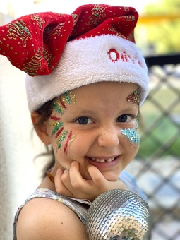 a little girl with a Santa hat holding a Christmas bauble with eco glitter on her face 