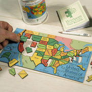 A hand on the left image holding Oregon, placing it into a partialy made States of America Jigsaw puzzle. At the top of the image is a tin and time records book