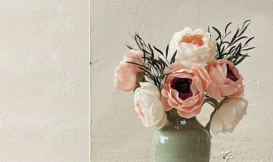 Close up of pink paper flowers in a green vase against a cream wall background