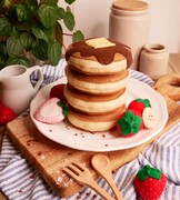 A stack of four pretend play felt food pancakes topped with syrup and butter surrounded by strawberries and banana slices.