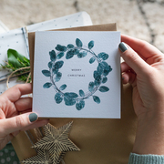 Eucalyptus wreath christmas card being held in front of christmas present