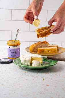 A jar of chutney with bread and cheese on a ktichen bench