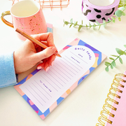 a to do list with a hand and pen about to write in their tasks for the day. the to do list is purple, lilac, nude and pink.
