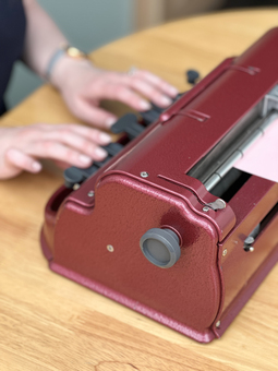 A close up of a red coloured Perkins brailler, with hands on the keys