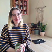 A photo of me sat at my desk, holding a mug of coffee, over top of the image are some digital illustrations and in the background there are a couple of plants.