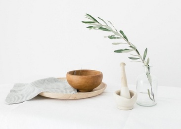 Olive branch, wooden bowl and pestle and mortar on a white table cloth