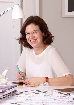 Business owner Kerri sitting at a desk, smiling, surrounded by paper stationery products.