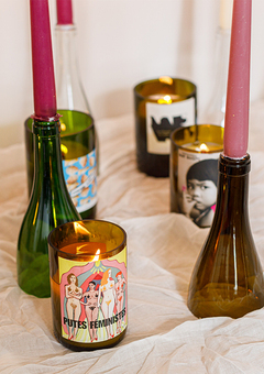 Wine bottle candles and candlesticks with candles in pink colours sitting on a piece of fabric on a table