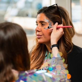 A glitter artist creating a glitter crescent shape around a woman's eye