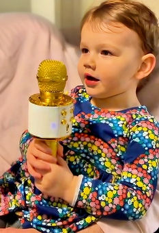  A happy child in a magical moment, celebrating her bespoke music birthday song designed just for her, singing into a golden microphone