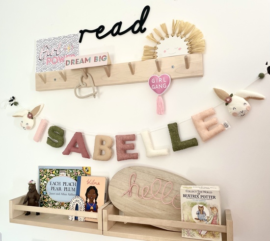name garland with bunnies hanging on a wall under a peg rail with other decorations and books