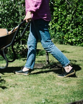 a woman wearing Poddy and Blacks using a wheel barrow in the garden 