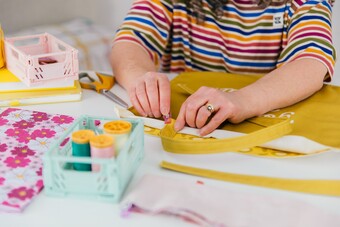 lady in a stripy top and head hairband pinning together a mustard coloured tote bag