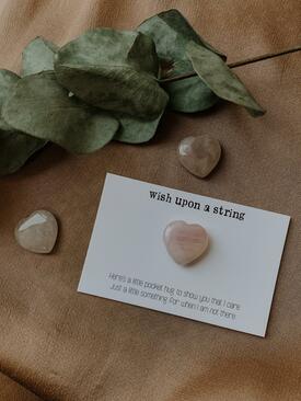 A Rose Quartz stone in the shape of a heart on a card with a motivational quote.