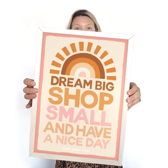 fabric banner hung next to a retro cabinet with a sunburst at the top and the words "DREAM BIG SHOP SMALL AND HAVE A NICE DAY" underneath in oranges and pinks