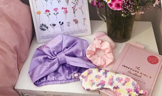 Bedside table lifestyle shot with lilac silk sleep cap, floral silk eye mask and pale pink silk scrunchie