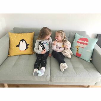 two little girls sharing a joke while seated on a sofa with two animal cushions for comfort