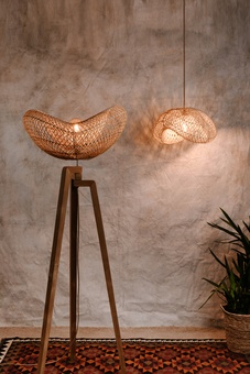 rattan and teak tripod floor lamp on colourful rug with large plant and a matching ratten ceiling shade